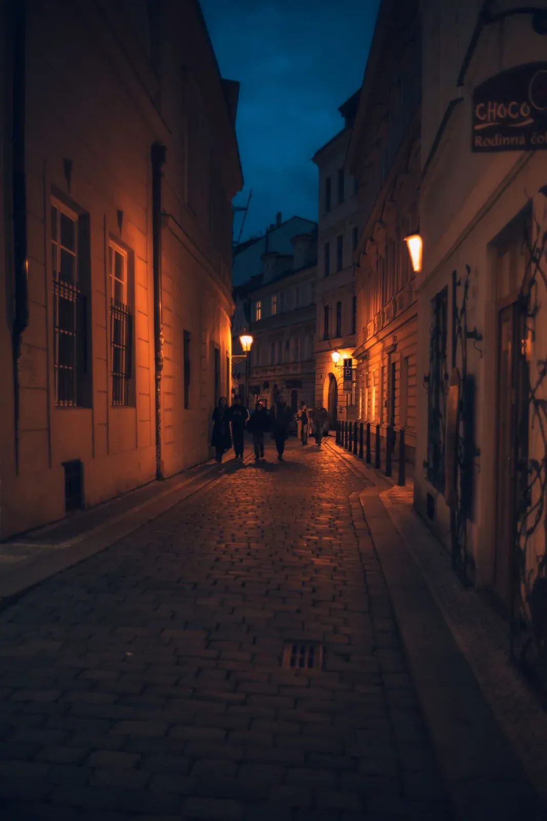 Persone che camminano di notte in un vicolo acciottolato illuminato di Praga.