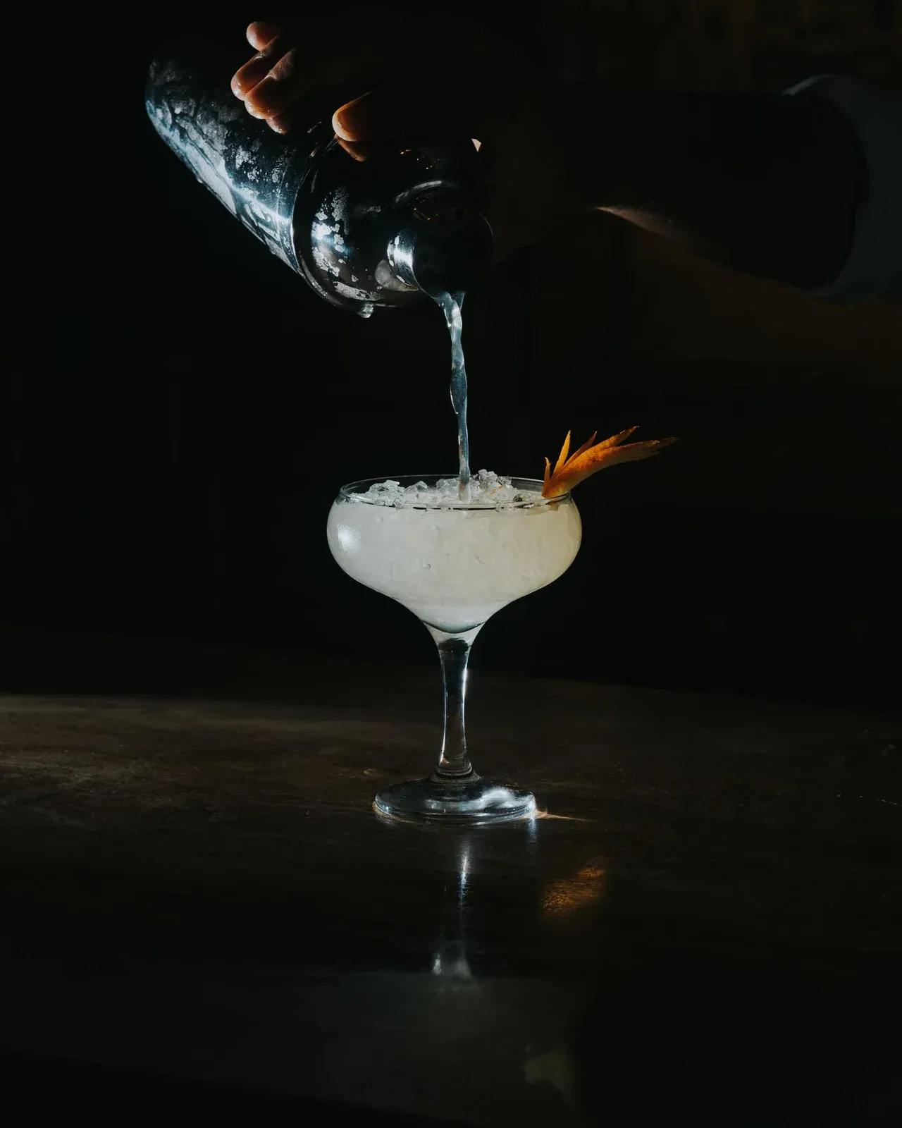 En bartender tilbereder en elegant cocktail i meget dæmpet lys.