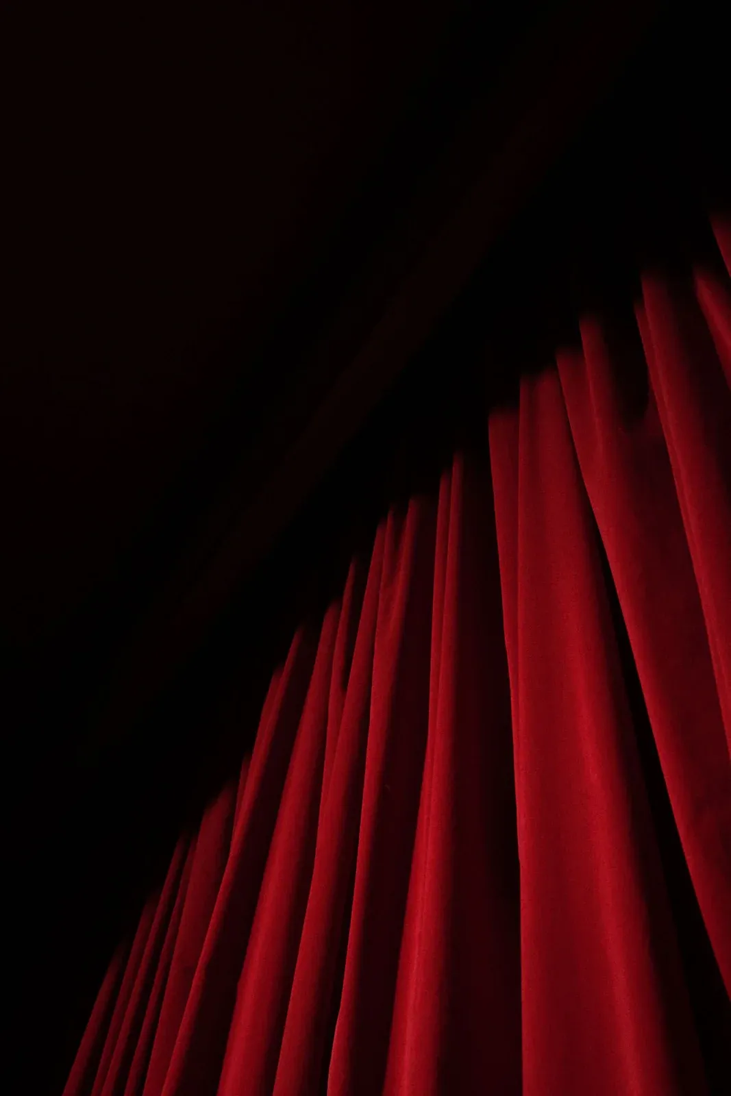 O cortină de teatru din catifea roșie, luminată de un reflector dramatic.