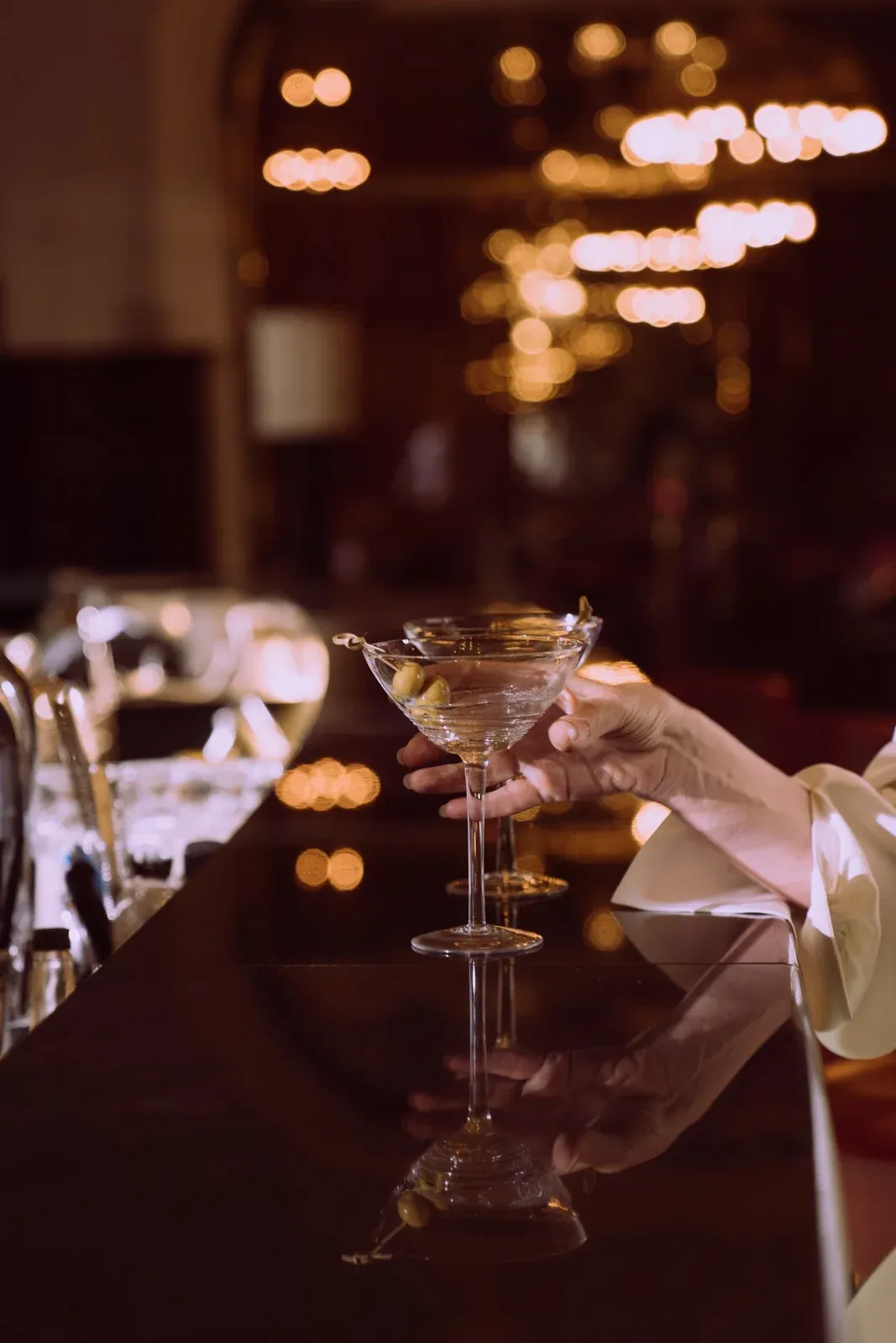 Die Hand einer Frau hält einen Martini in einer eleganten, gedämpft beleuchteten Bar.
