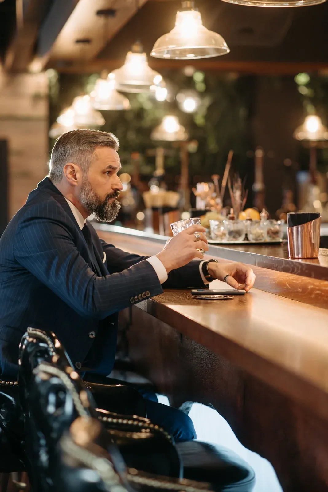 Ein Mann im Anzug hält an einer eleganten Bar ein Getränk.